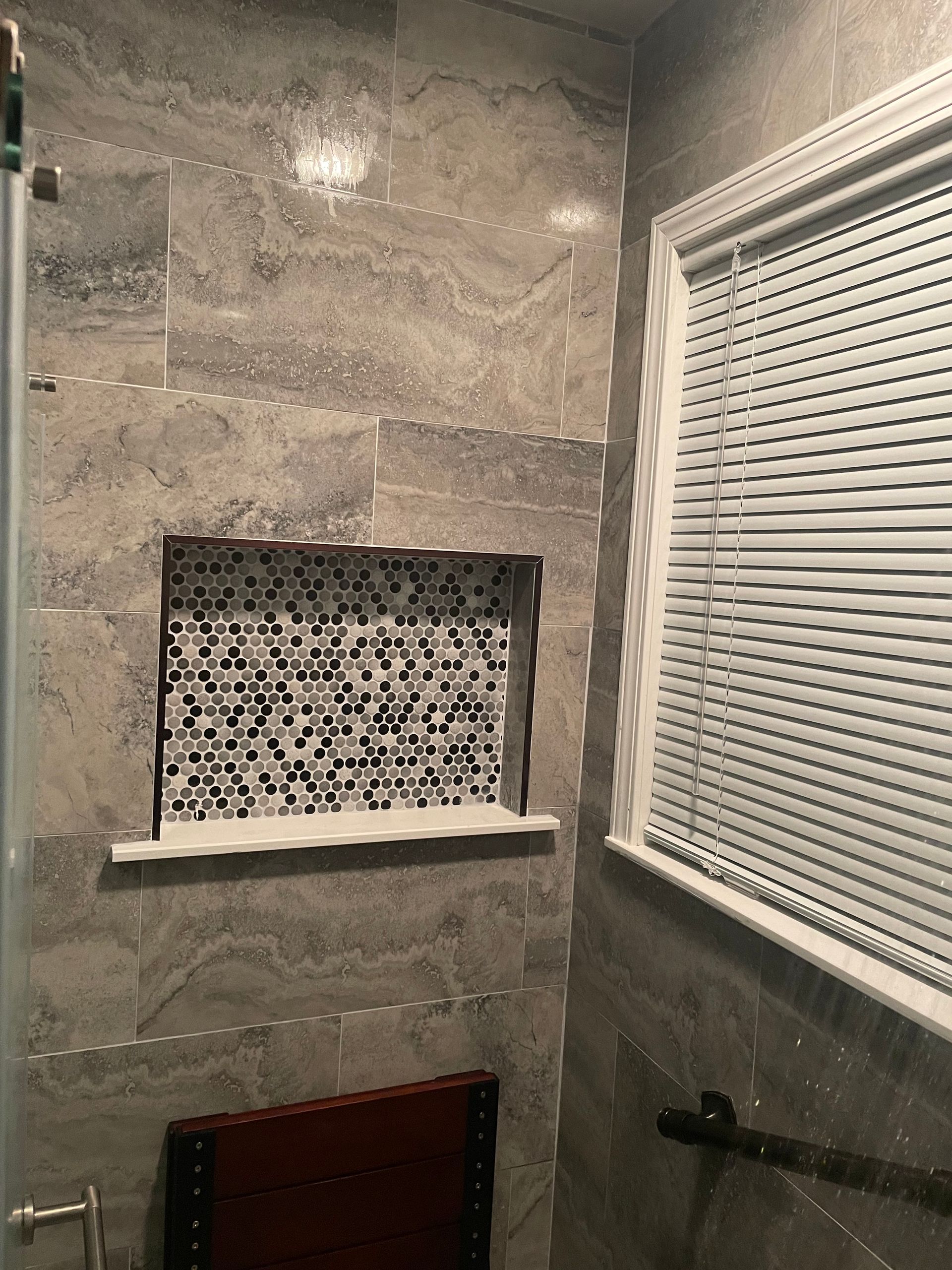 Bathroom shower with gray tile, a recessed shelf, and a window with white blinds