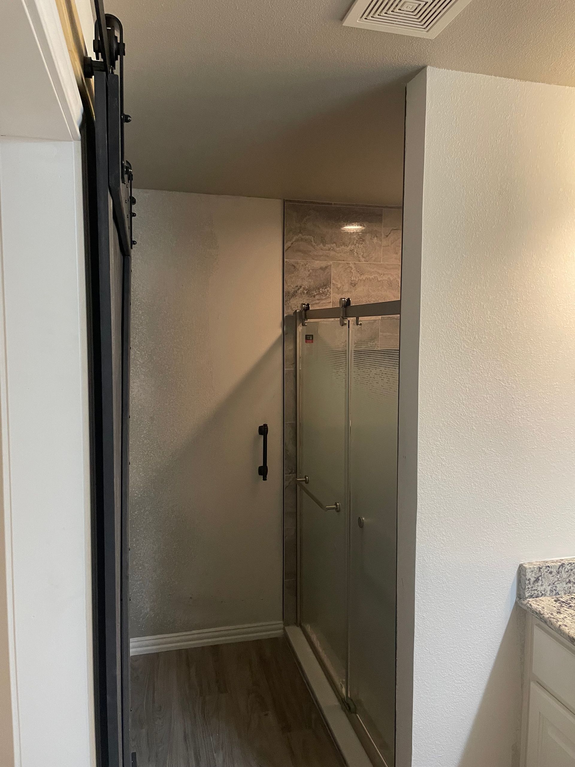 Narrow hallway with a glass shower stall and beige walls in a small bathroom area