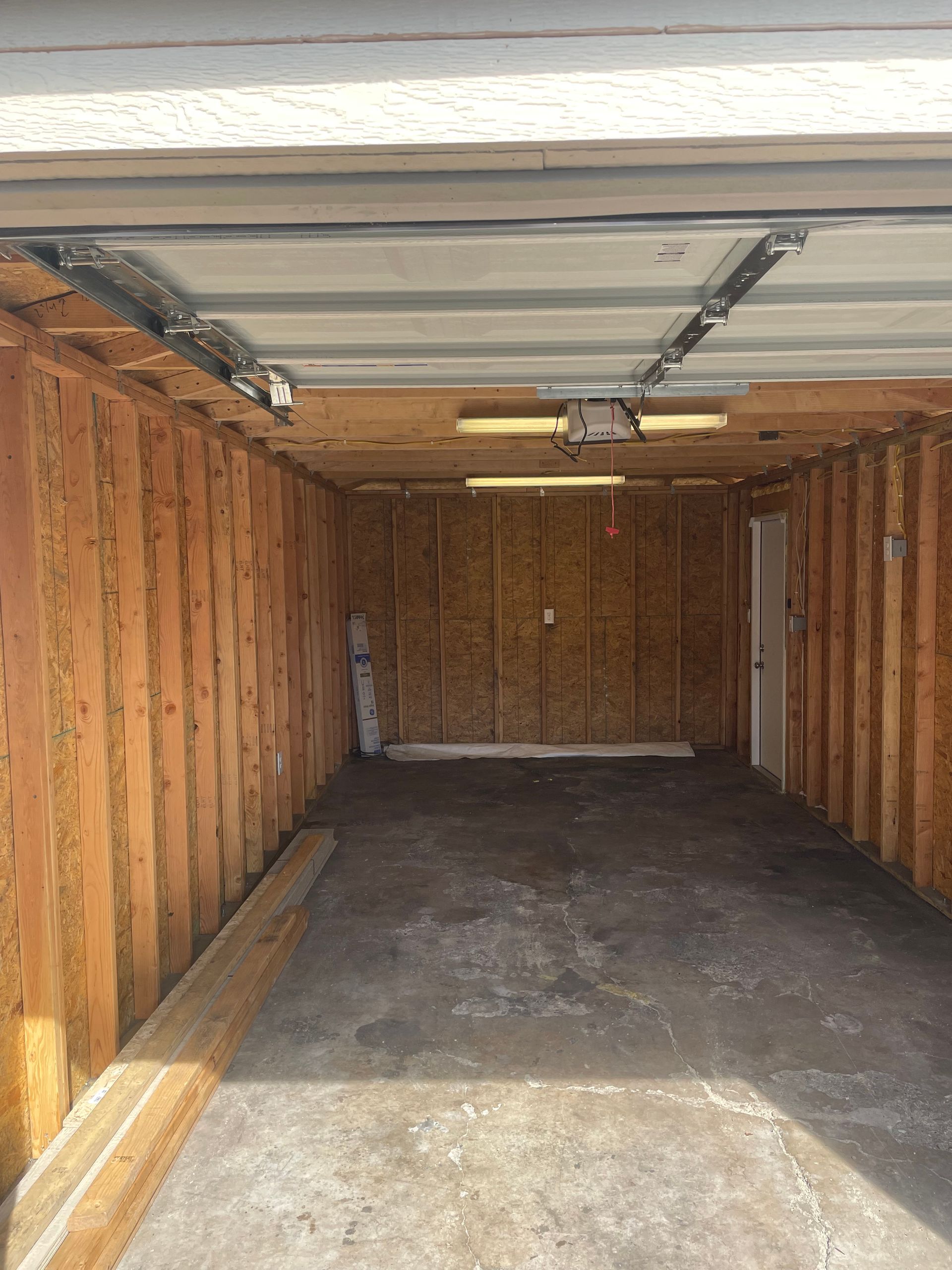 Empty wooden garage with unfinished walls, concrete floor, and open overhead door.