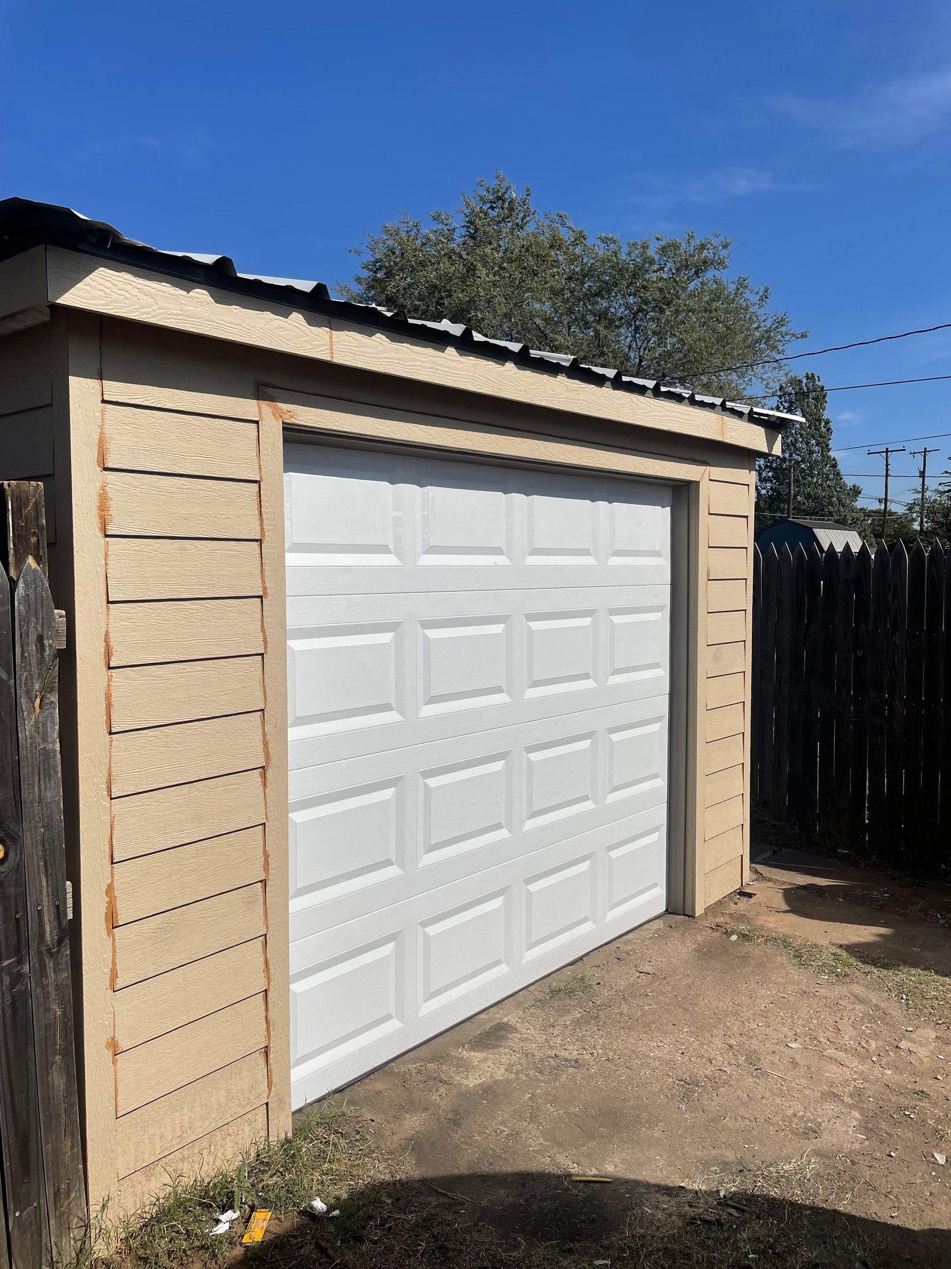 Detached garage with a white paneled door and tan stone siding in a sunny yard