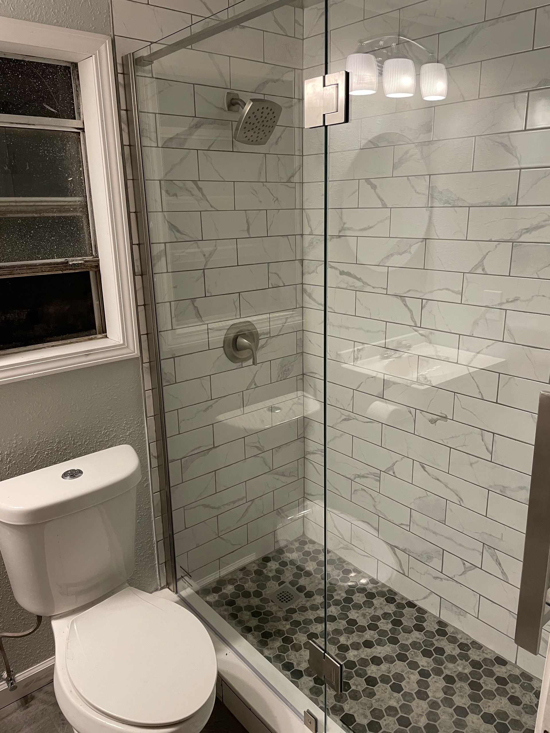 Modern bathroom with glass walk-in shower, white toilet, gray tile, and mosaic shower floor.