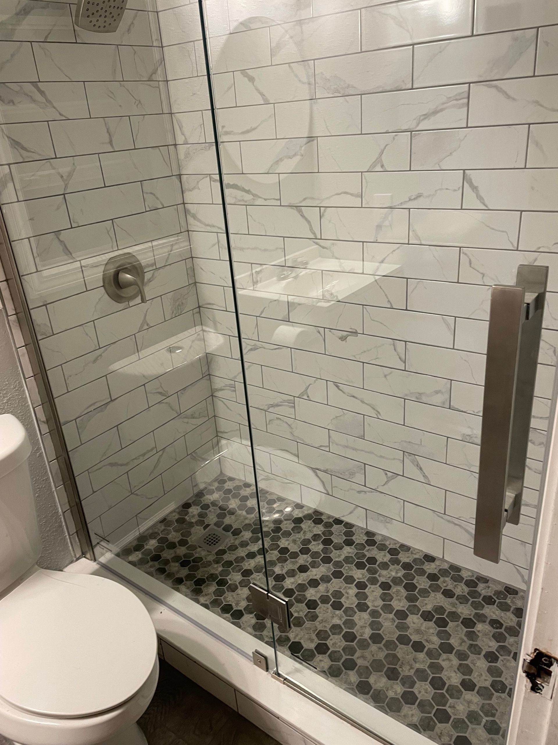 Small bathroom with glass shower enclosure, white subway tiles, mosaic shower floor, and toilet visible.