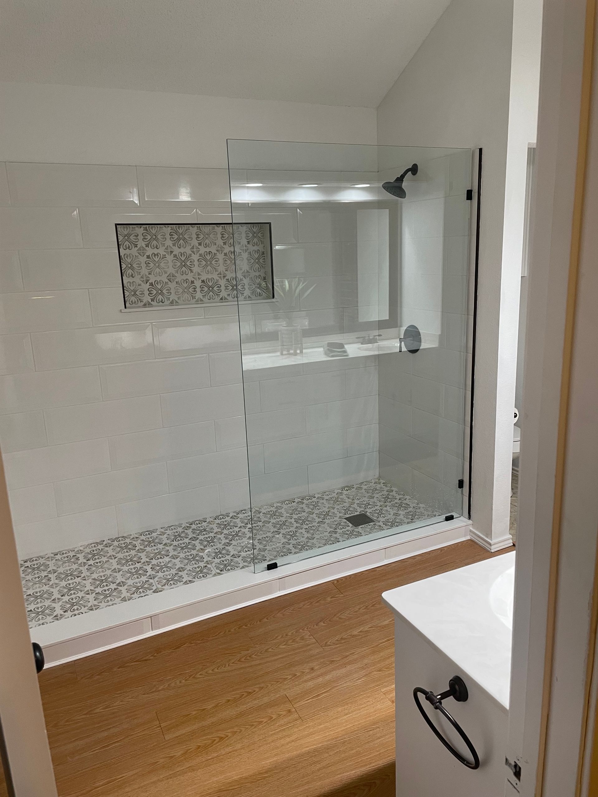 Modern bathroom with glass shower enclosure, mosaic tile accents, and wood-look floor.