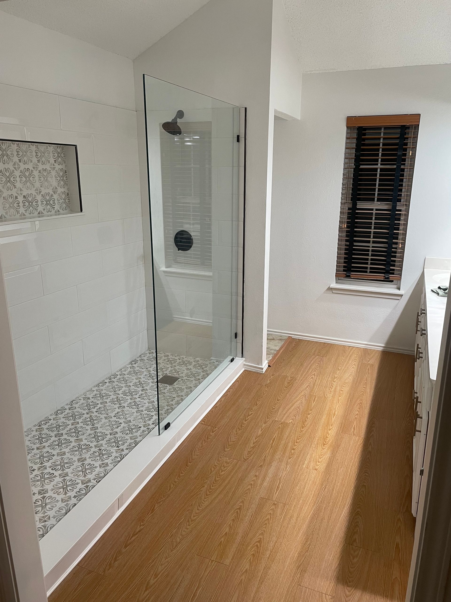 Modern bathroom with walk-in shower, glass partition, white tile, and a wood floor.