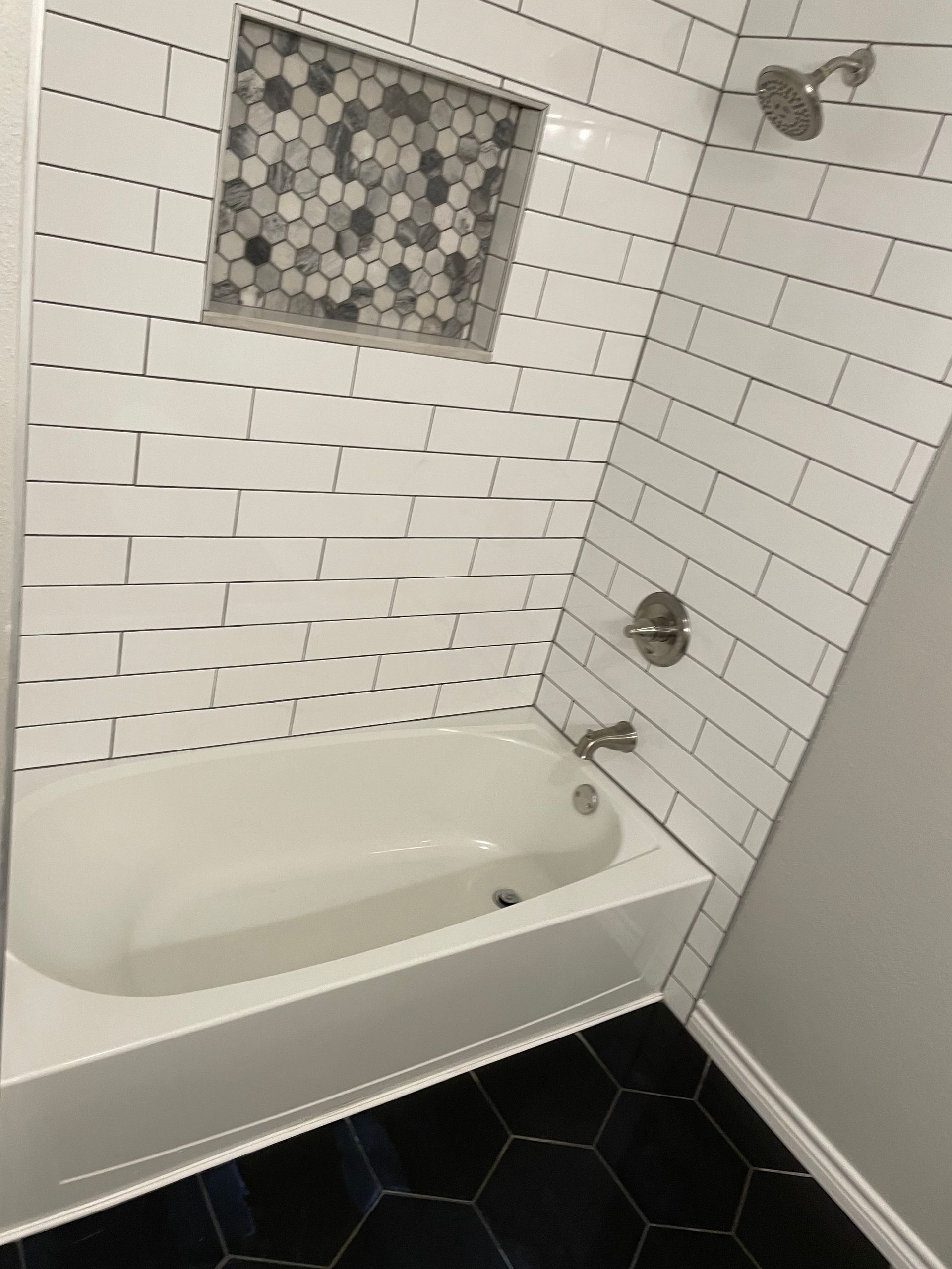 White tiled bathroom with a bathtub, mosaic accent tile, chrome fixtures, and dark hexagon floor tiles