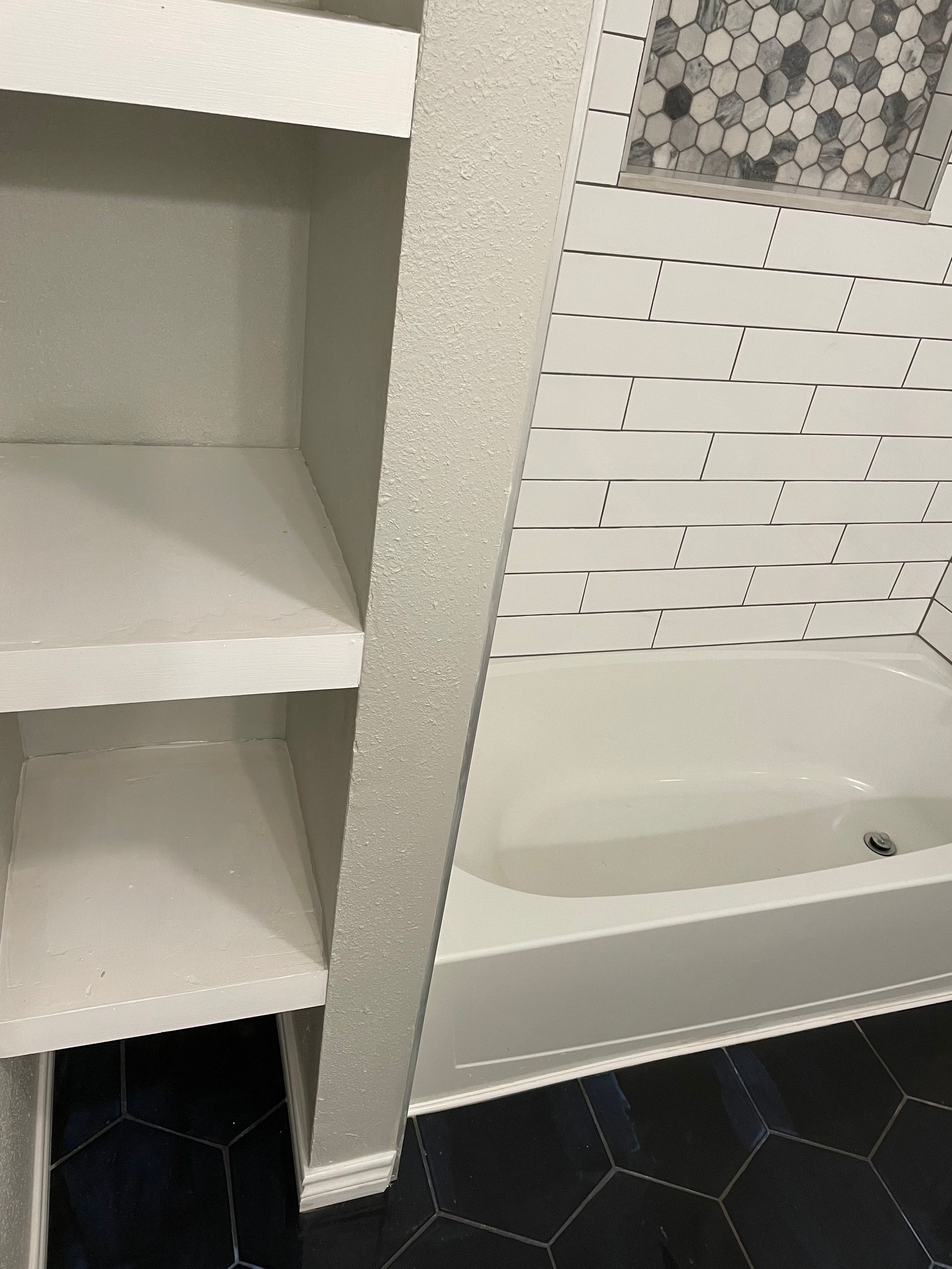 Open white bathroom shelves beside a white sink and patterned tile wall.