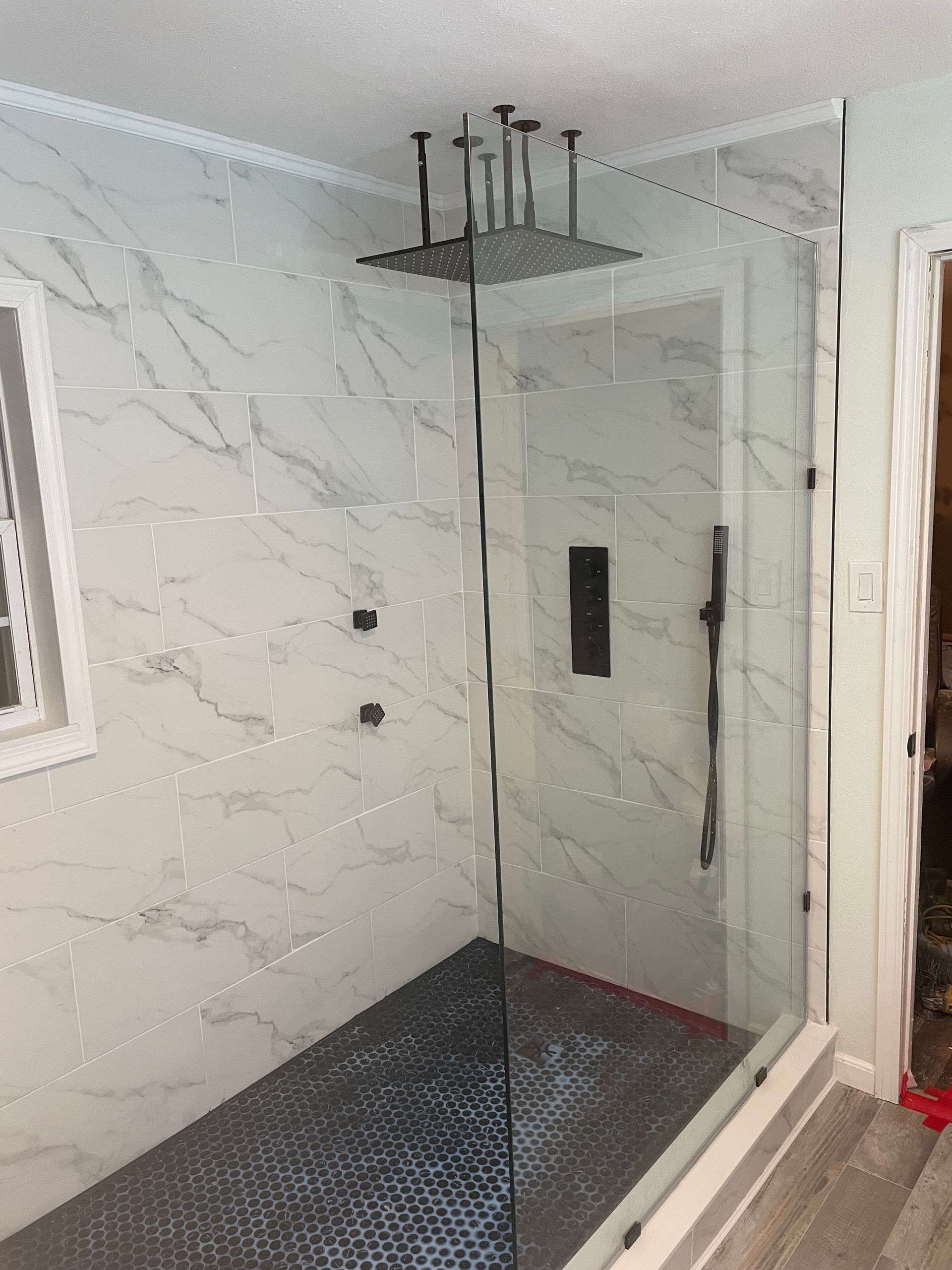 Modern shower with glass enclosure, marble walls, and black rain showerhead