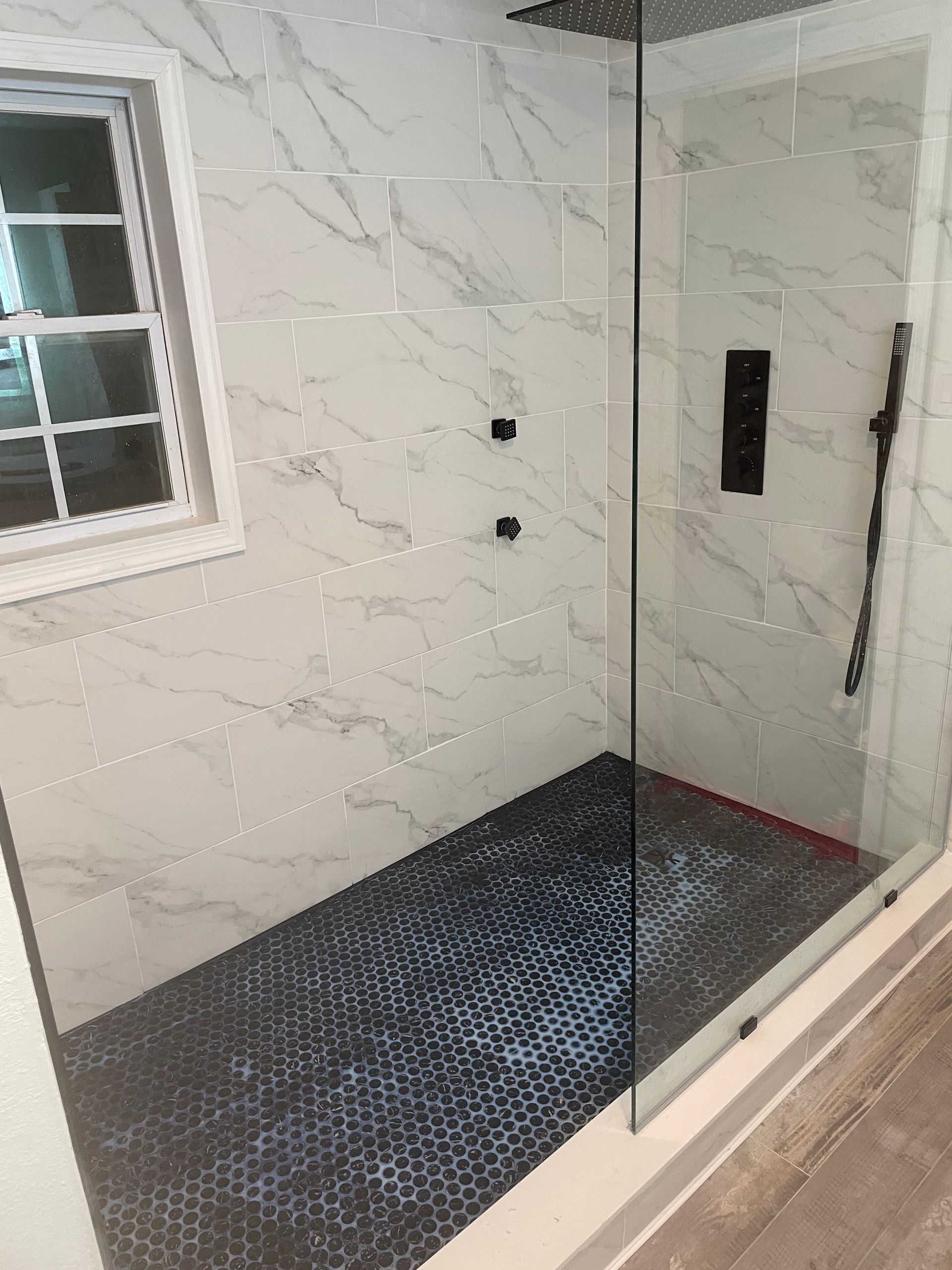 Modern shower with marble-pattern tile, glass door, dark floor, and small window