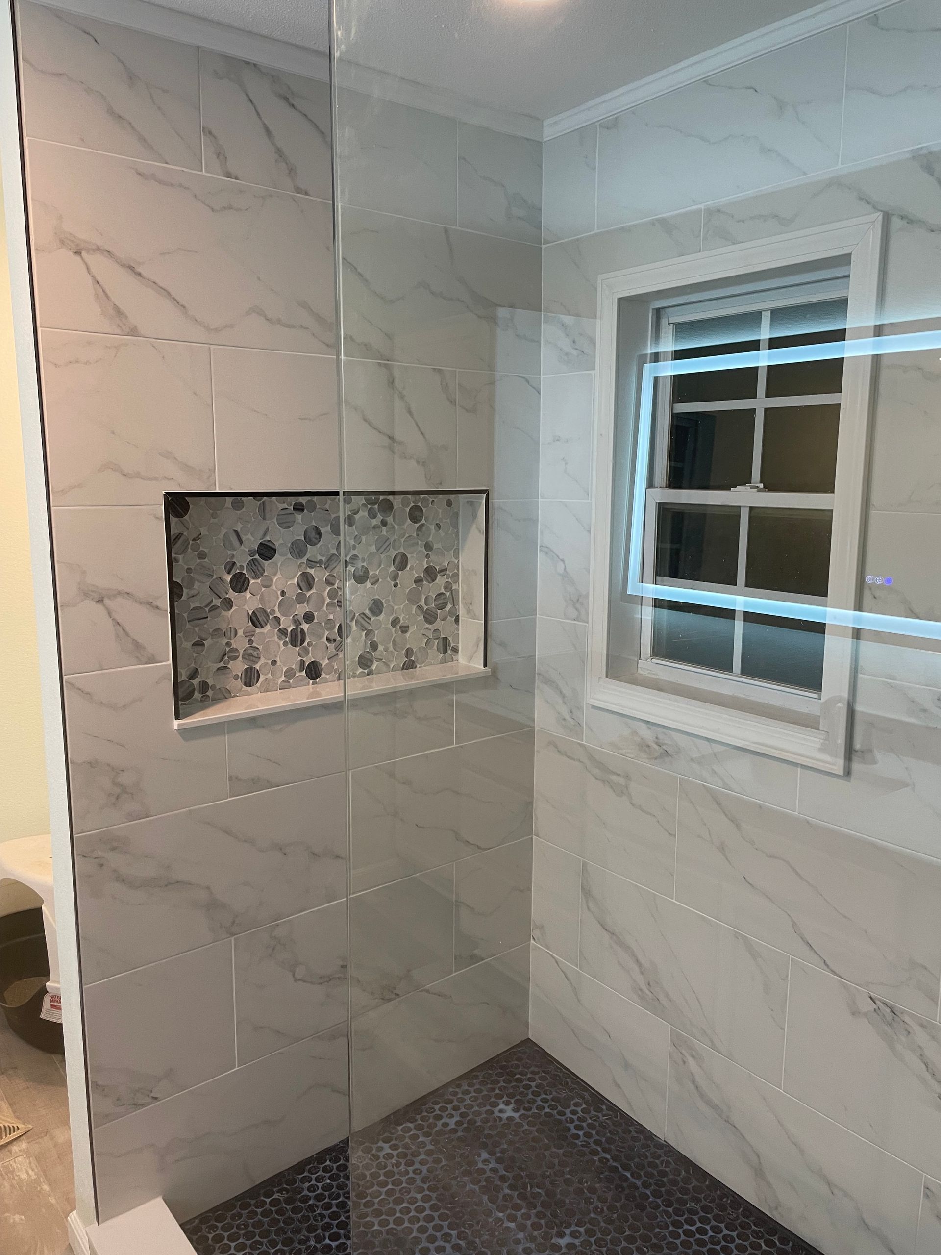 Tiled shower with a recessed shelf, dark floor tiles, and a small window on the right.