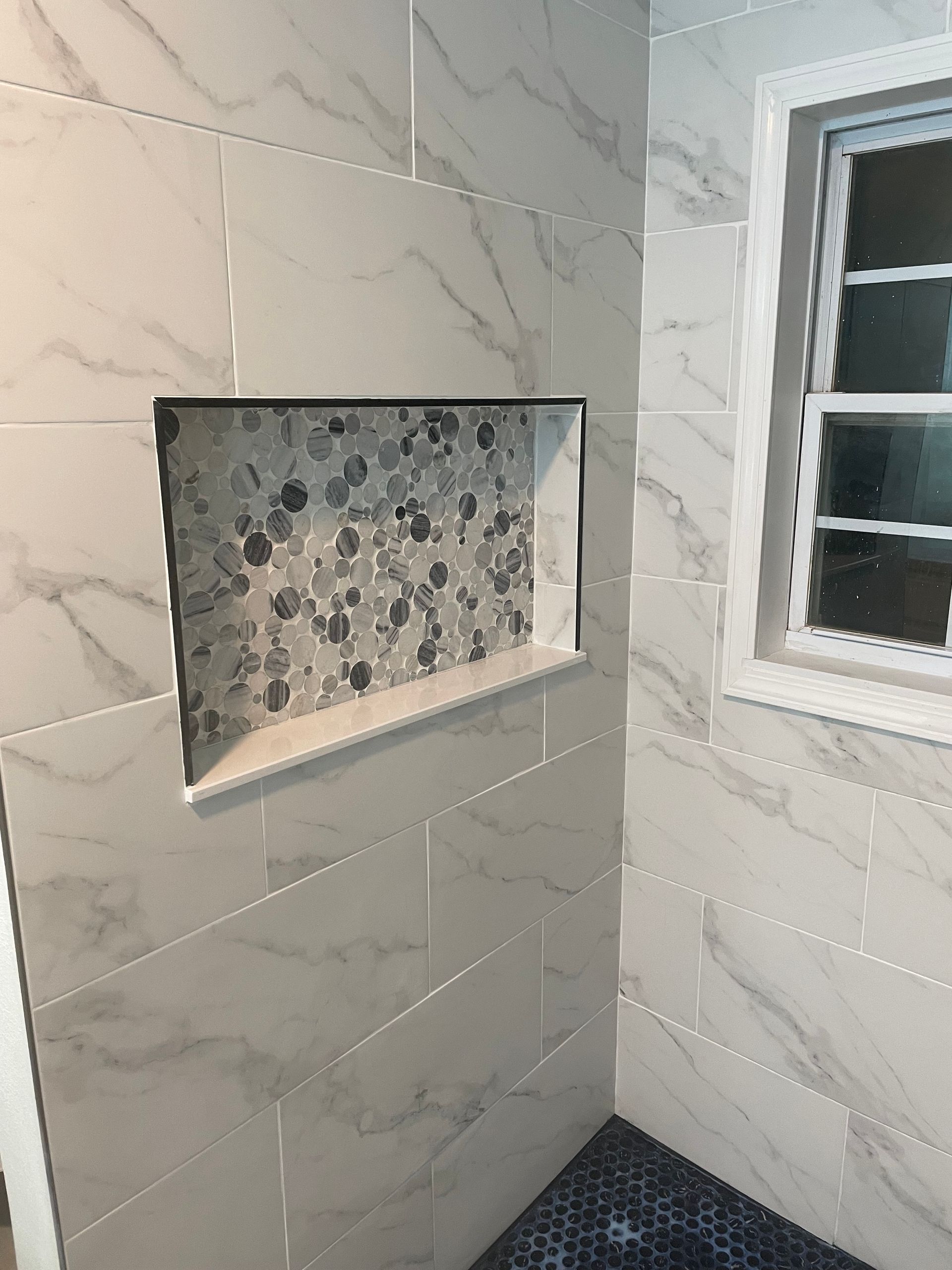 Walk-in shower with tiled walls, recessed shelf, and a window on the right