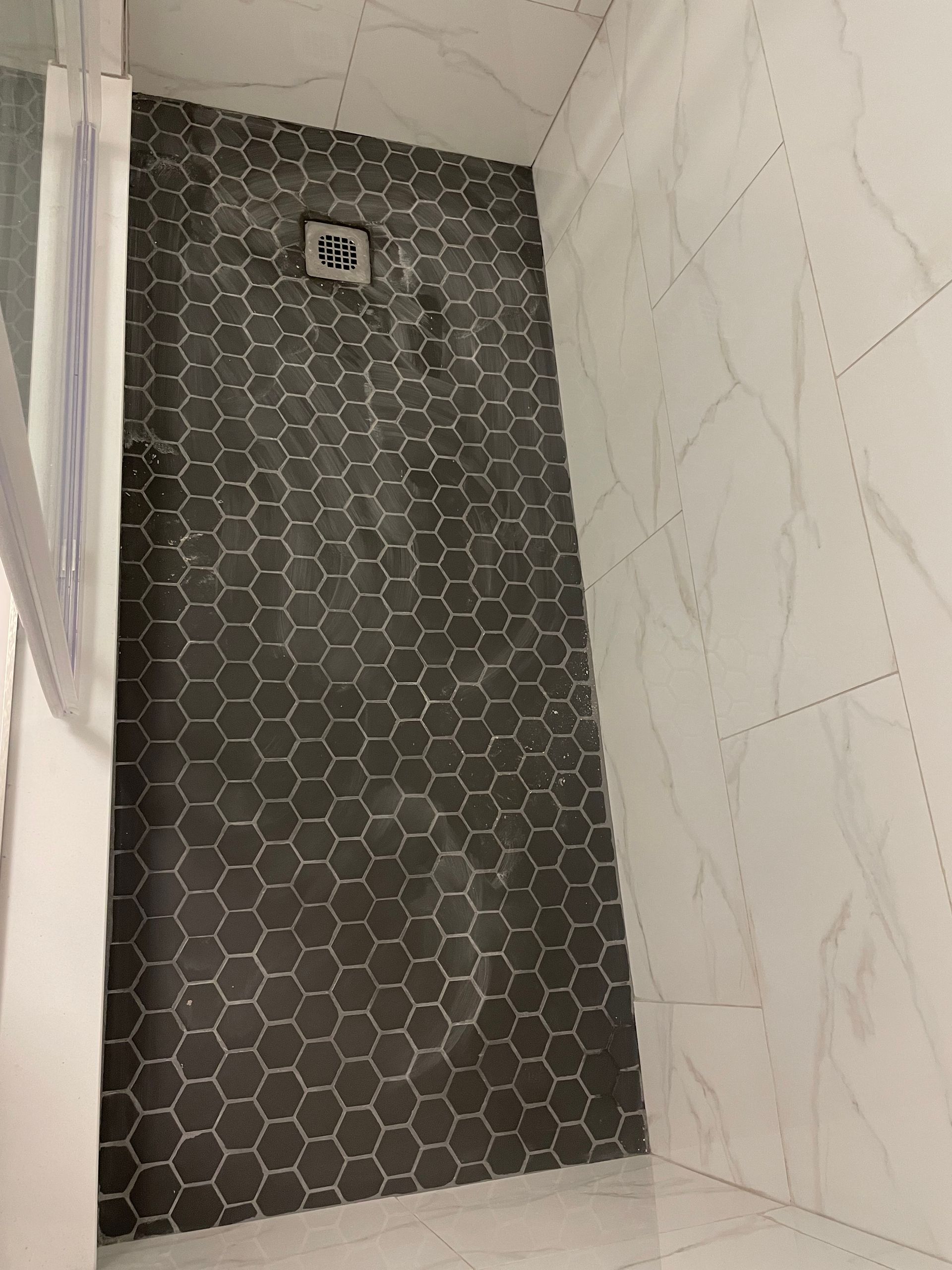 Tiled shower stall with dark hexagon accent wall and white marble-pattern walls