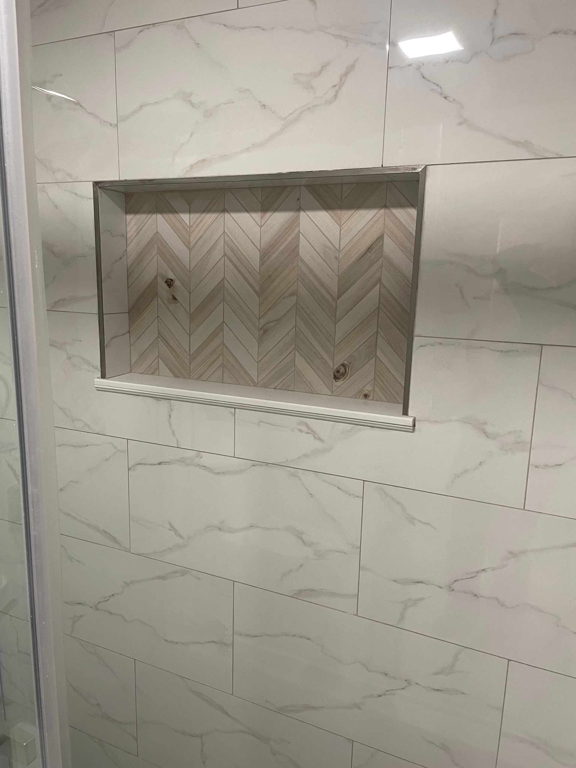 Tiled wall with a recessed decorative niche in a chevron pattern and a dotted trim line beneath it