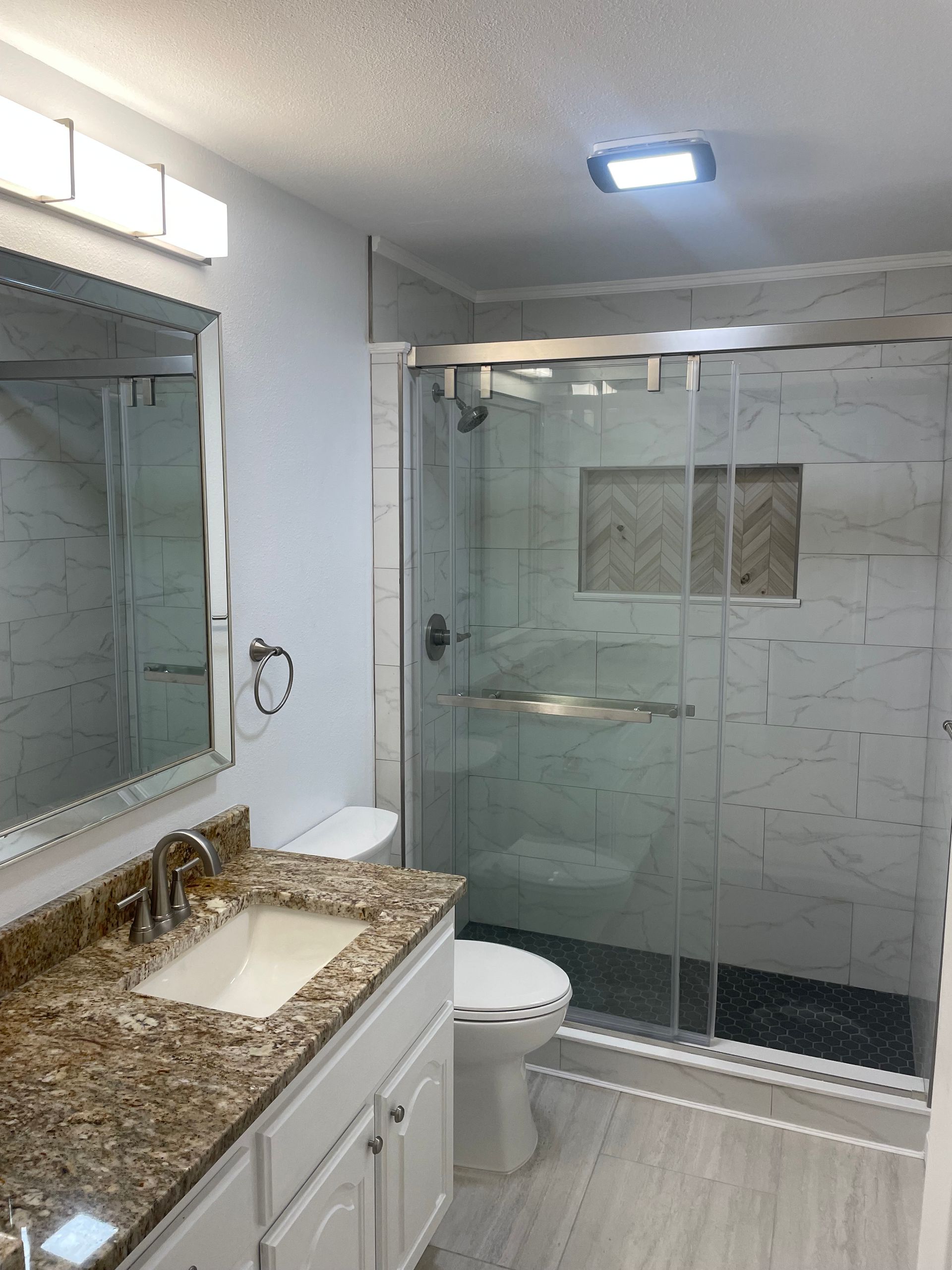 Modern bathroom with granite vanity, large mirror, toilet, and glass-enclosed shower.