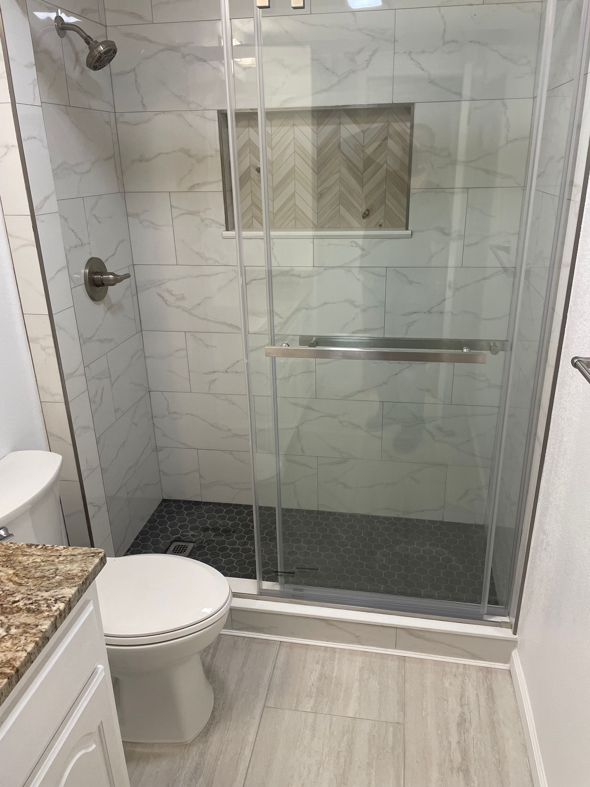 Small bathroom with glass shower, toilet, and granite countertop vanity.