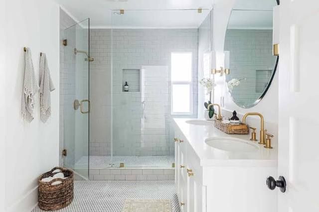 Bright white bathroom with glass shower, double sinks, and brass fixtures