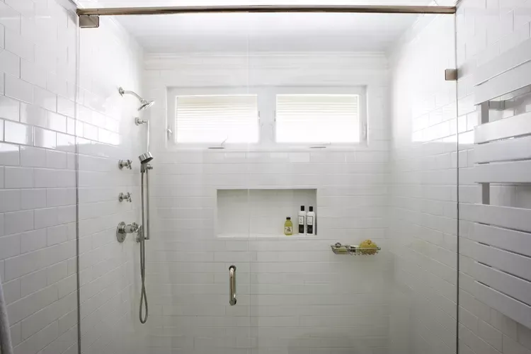 Bright white tiled walk-in shower with double windows and chrome fixtures