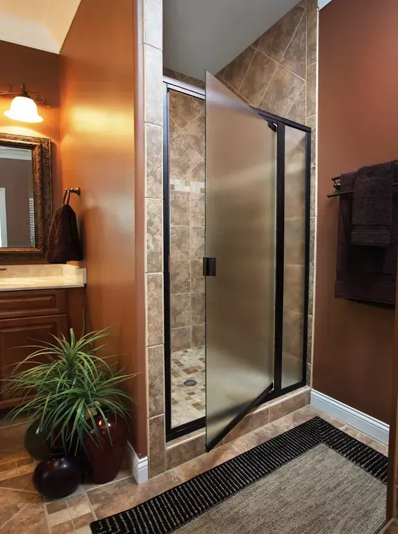 Bathroom with glass shower door, tan tile, brown walls, a sink area, and a black towel rack.