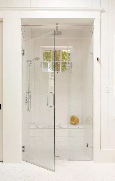 Glass shower enclosure in a bright white bathroom with a tiled bench and shower fixtures