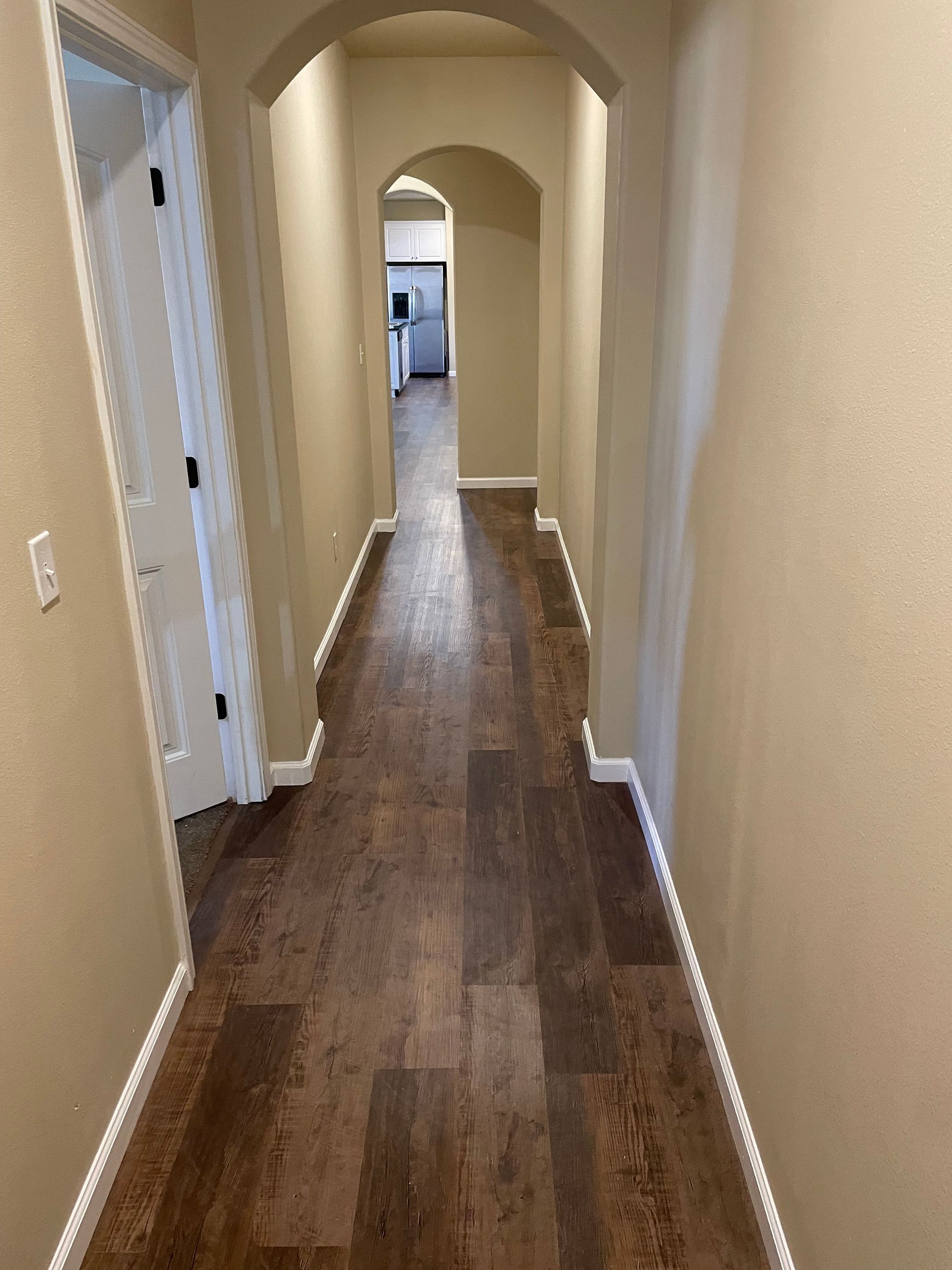 Narrow beige hallway with wood floors and arched doorway leading to another room.