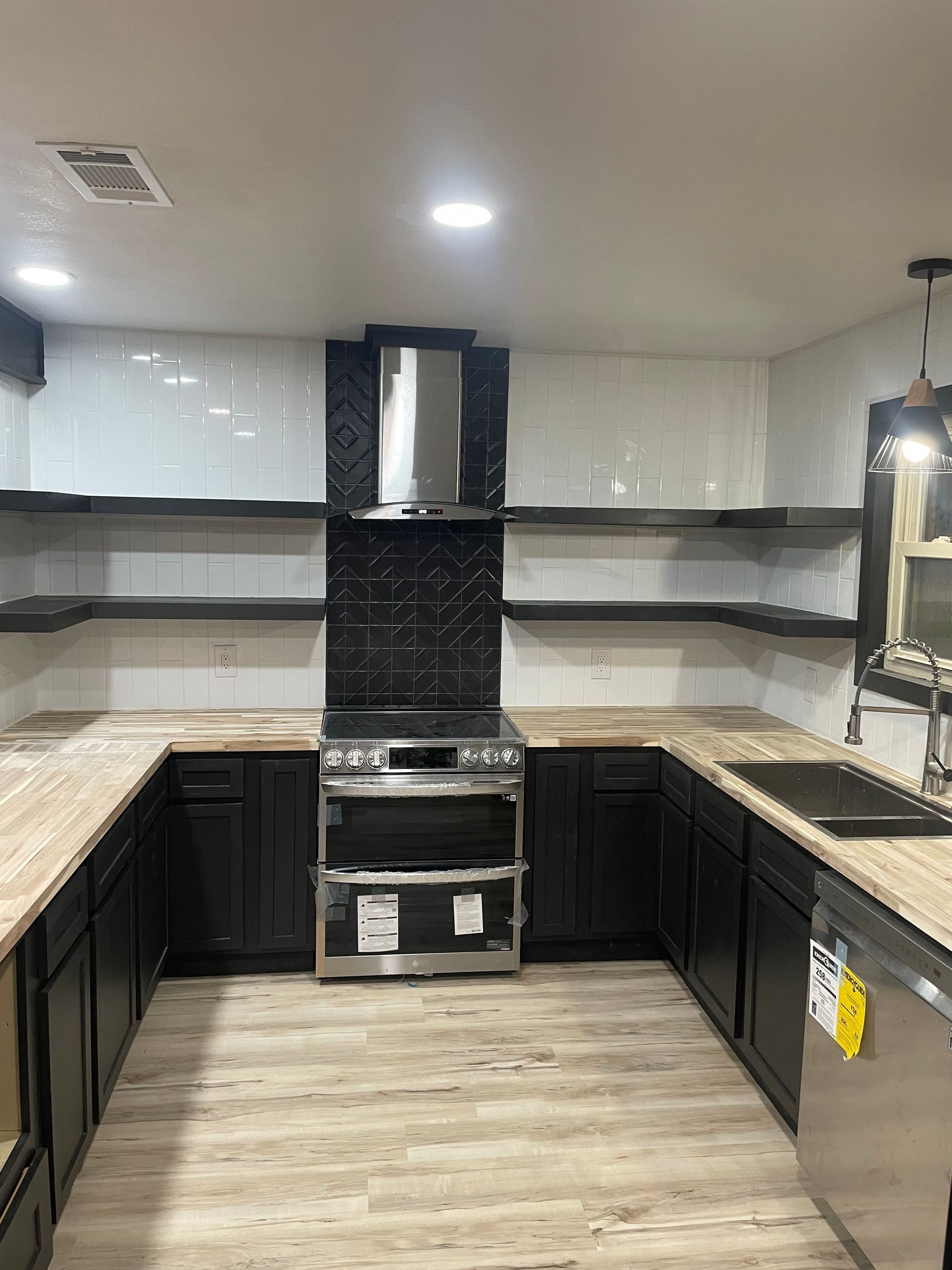 Modern kitchen with dark cabinets, light countertops, black backsplash, and stainless steel stove and hood