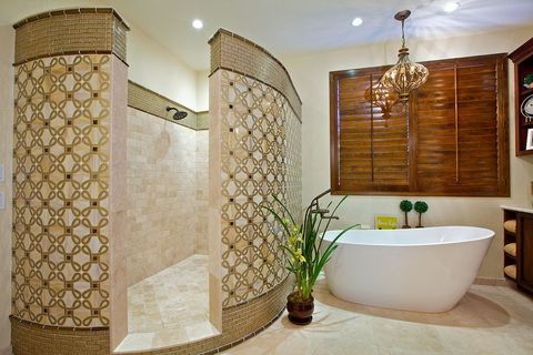 Luxurious bathroom with tiled curved shower, freestanding tub, wood blinds, and potted plant