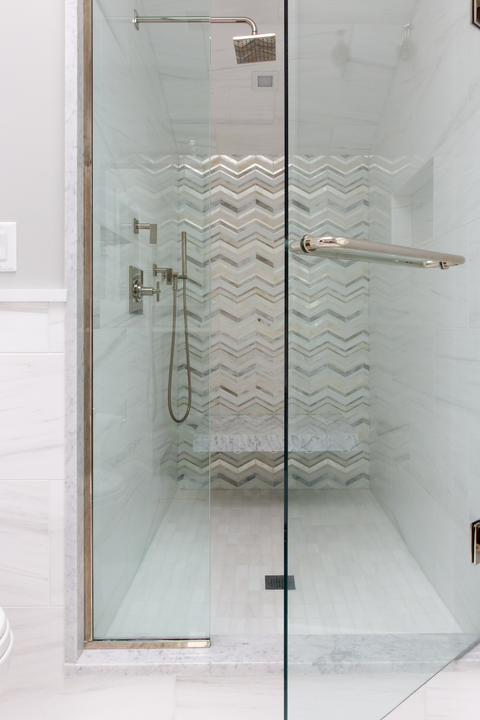 Glass shower enclosure with chrome fixtures and herringbone tile wall inside a bright bathroom
