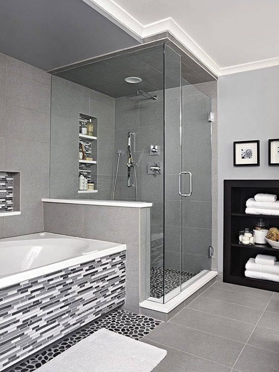 Modern gray bathroom with glass shower, tiled tub, and black shelving unit