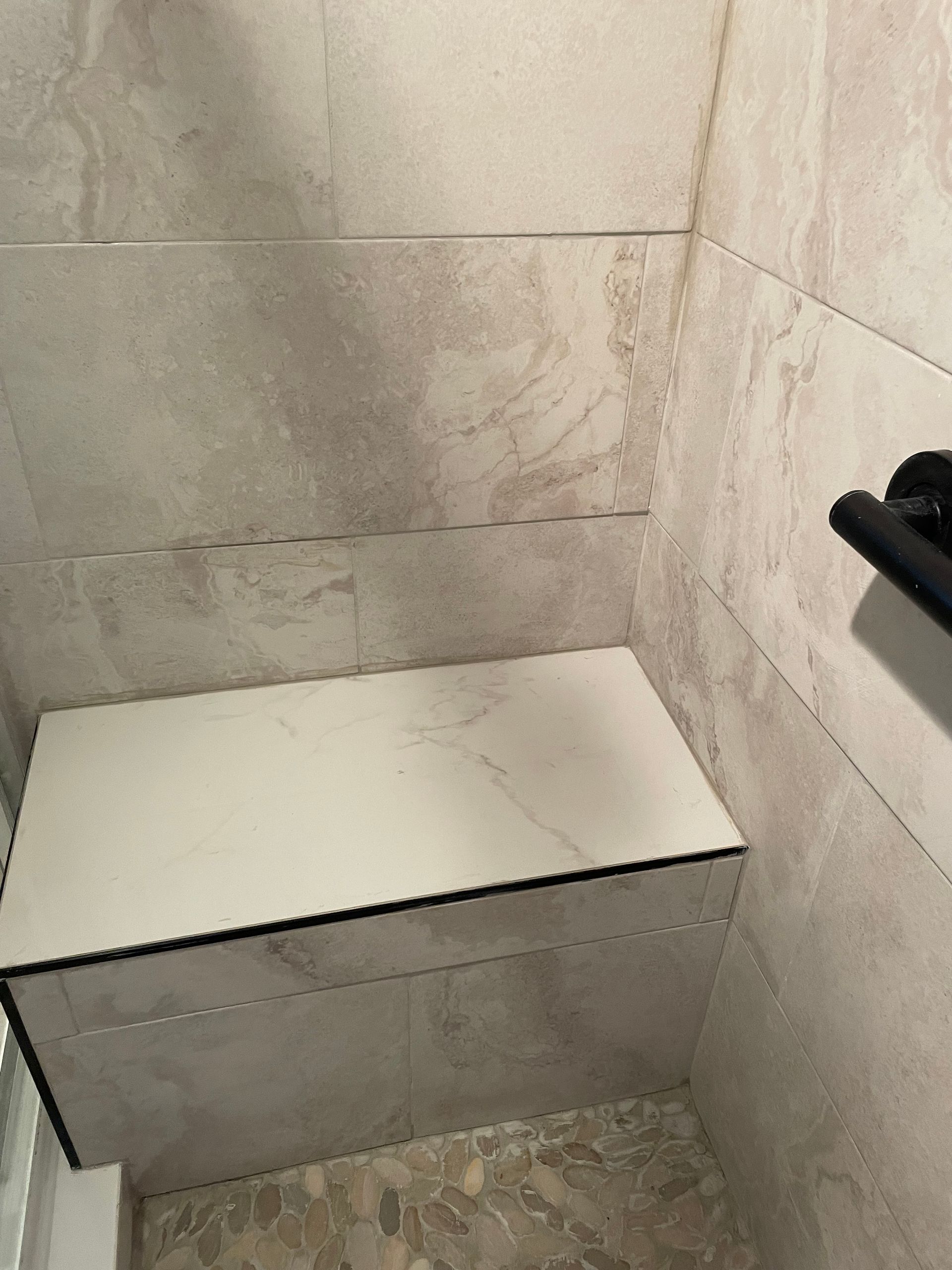 Small white wall-mounted toilet or bench in a beige tiled bathroom stall