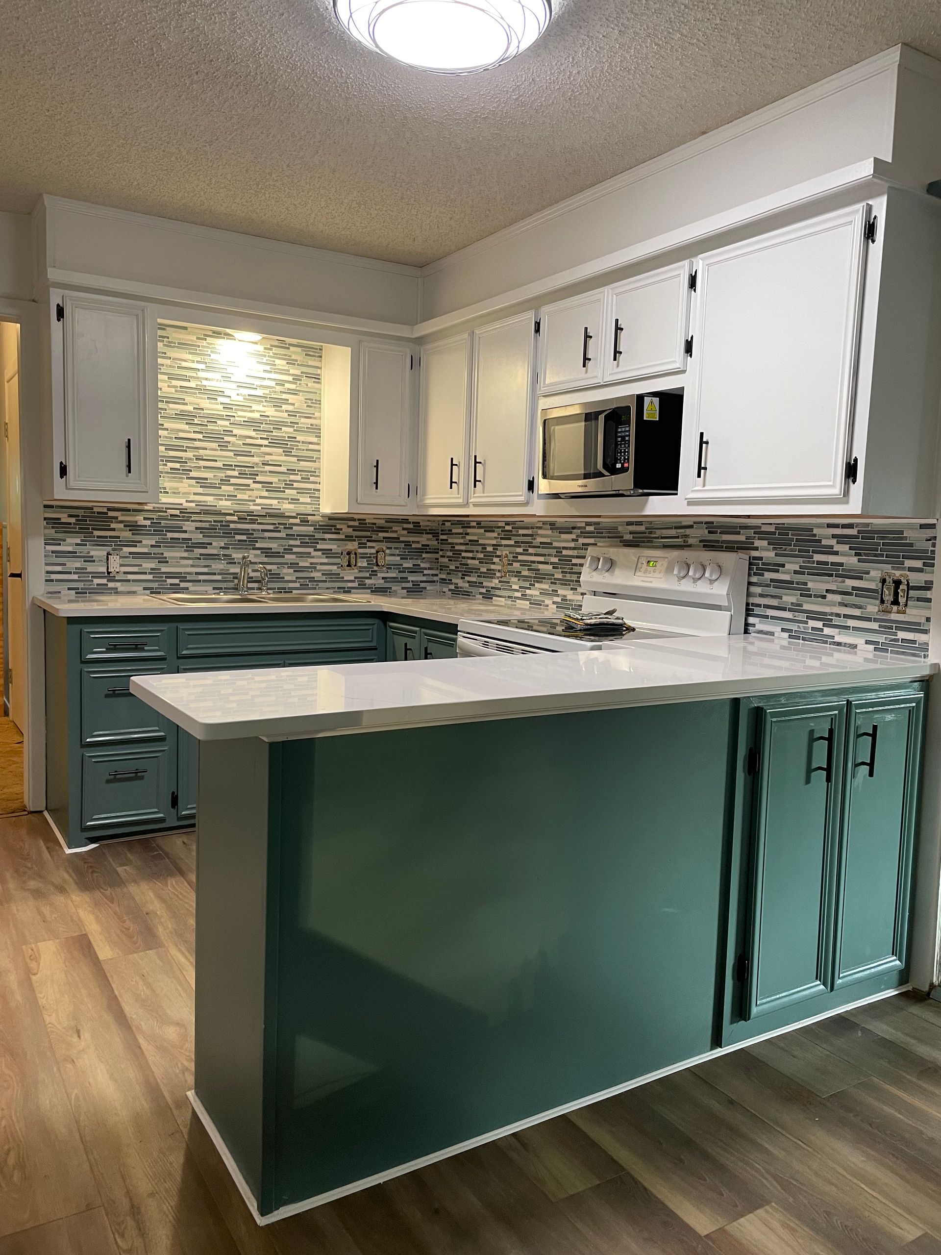Teal kitchen island with white countertops and cabinets, mosaic tile backsplash, and wood flooring.