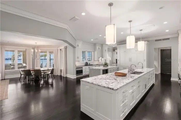Modern open-concept kitchen and dining area with dark floors, white cabinetry, marble island, and pendant lights