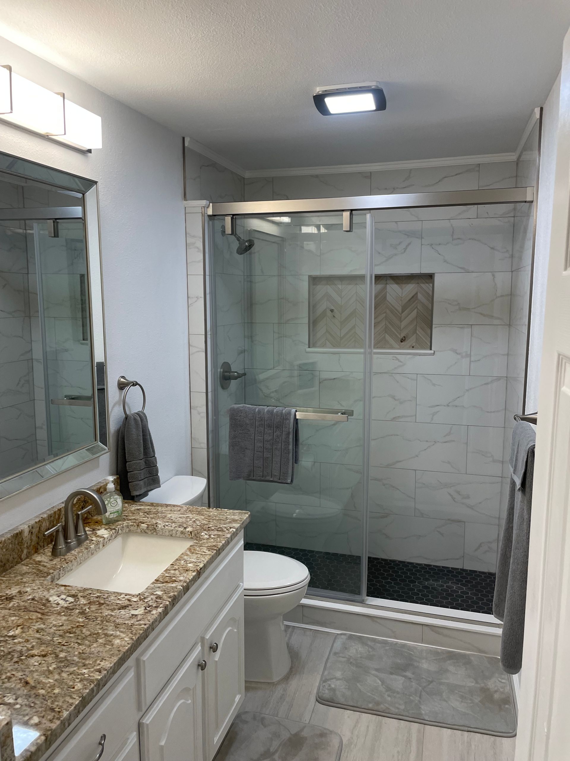 Bathroom with granite vanity, mirror, toilet, and glass-enclosed shower with tiled walls
