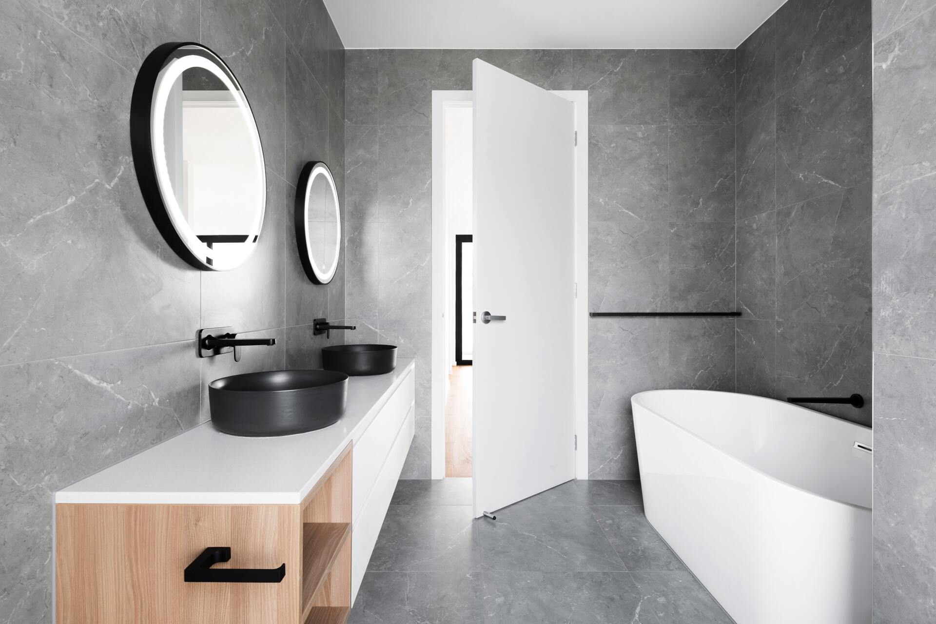 Modern gray bathroom with double vanity, round mirrors, and a white freestanding bathtub