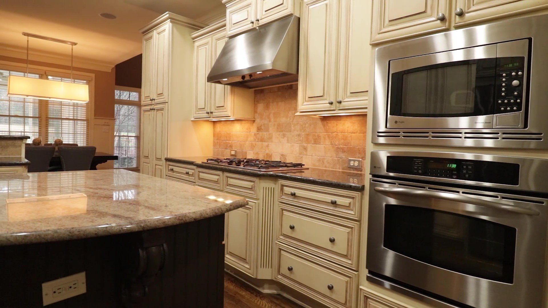Modern kitchen with granite island, cream cabinets, and built-in stainless steel oven and microwave