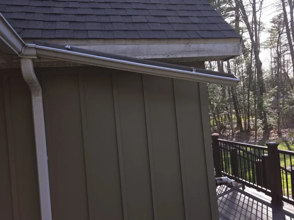 Green-sided building with dark roof, white gutters hanging off in need of repair
