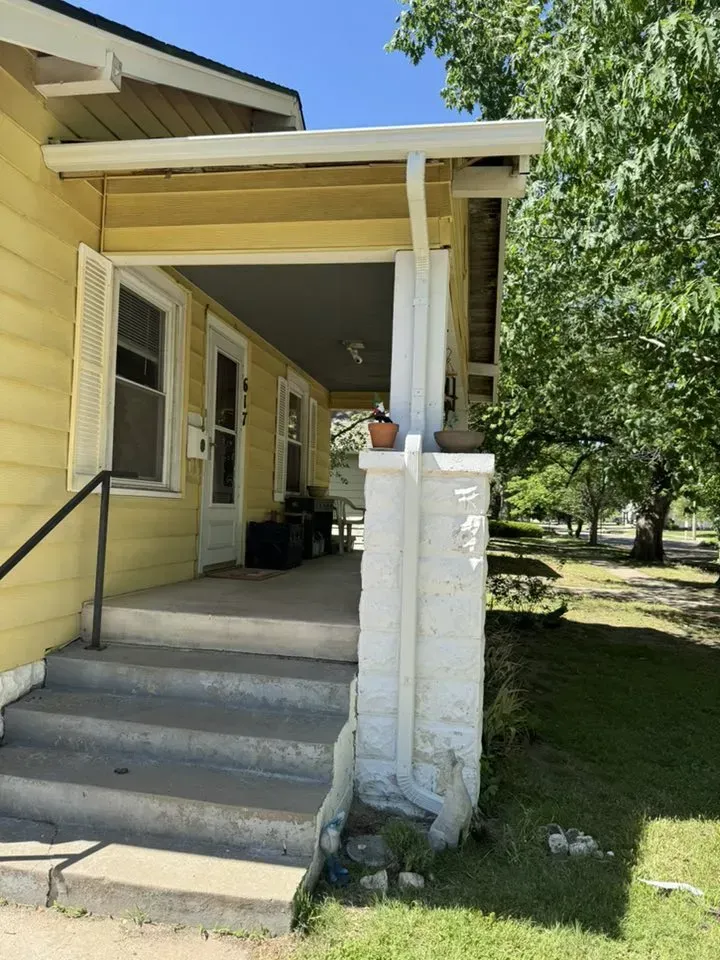 Yellow Andover KS home with new white gutters showing on porch on a sunny day