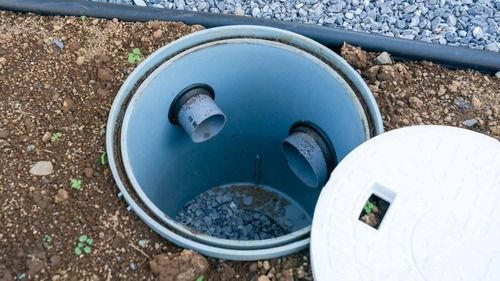 Close up of an open drywell in the dirt with pipes running inside