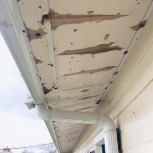 Damaged soffit and gutter on a cream-colored house. Peeling paint and water stains are visible.