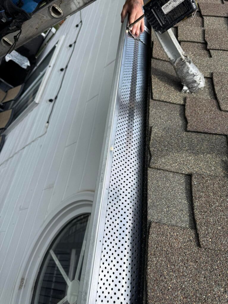 Man installing perforated metal gutter guard on a house roof.