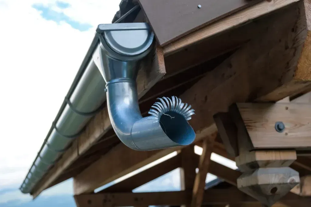 Gutter with a downspout on a wooden roof, directing water.