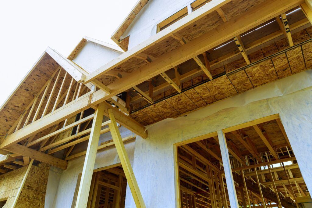 Wooden house under construction, view from below. Framing, roof beams, windows, bright sky.