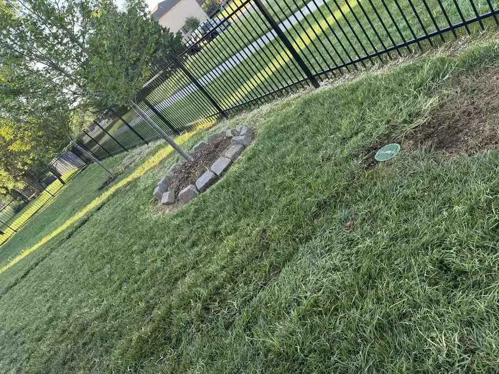 After pic of a newly covered underground drain, lawn with a black fence.