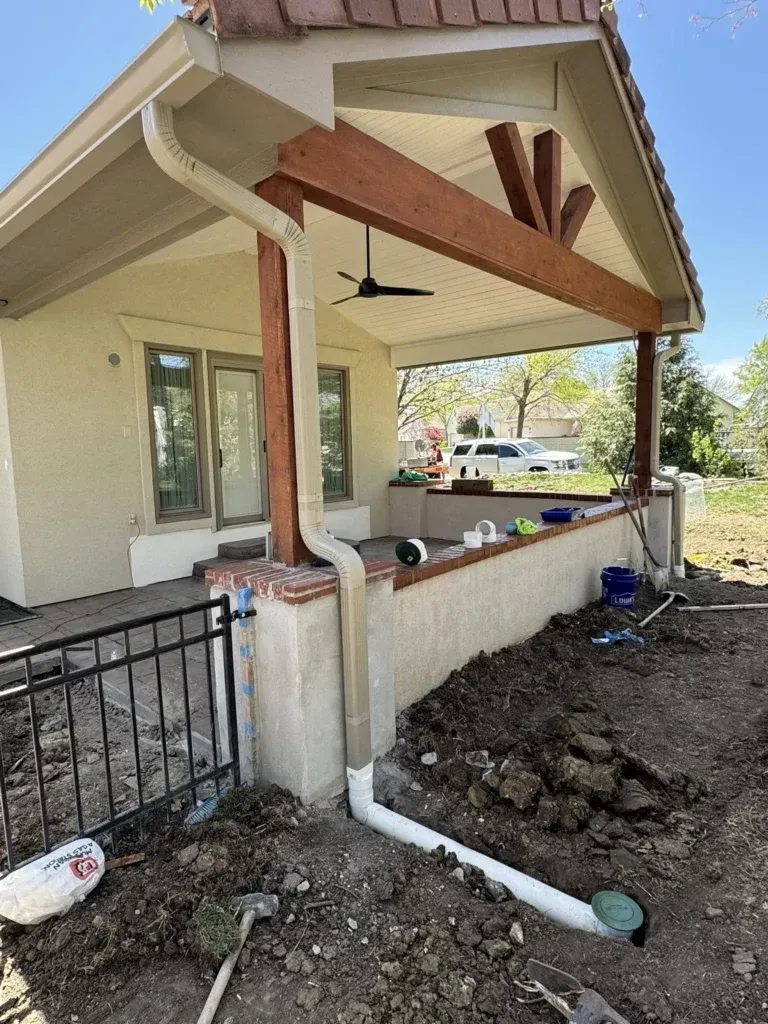tan downspout off the side of a house leading into a white underground drain