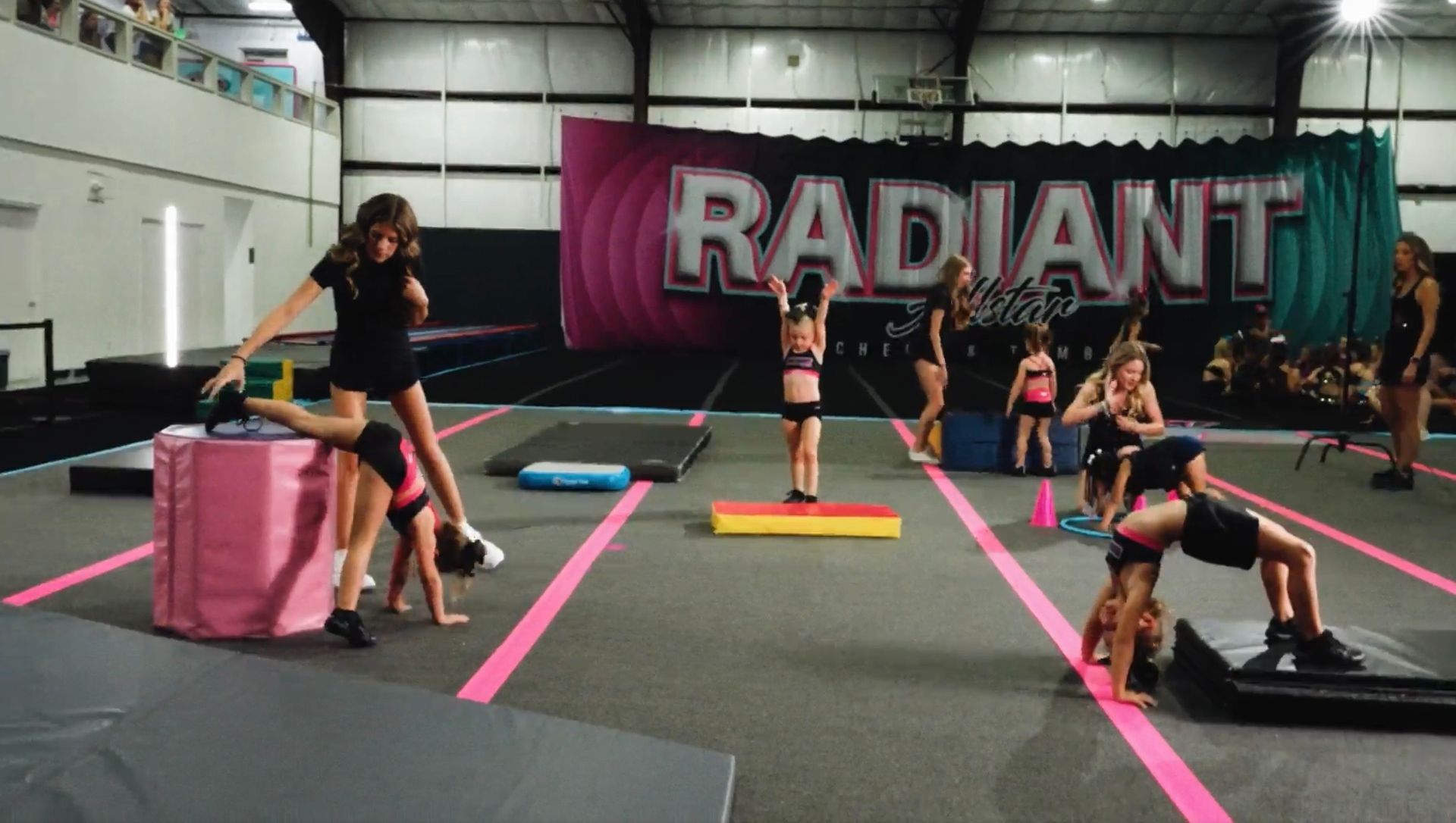 A woman is helping a little girl do stretching exercises on a yoga mat.