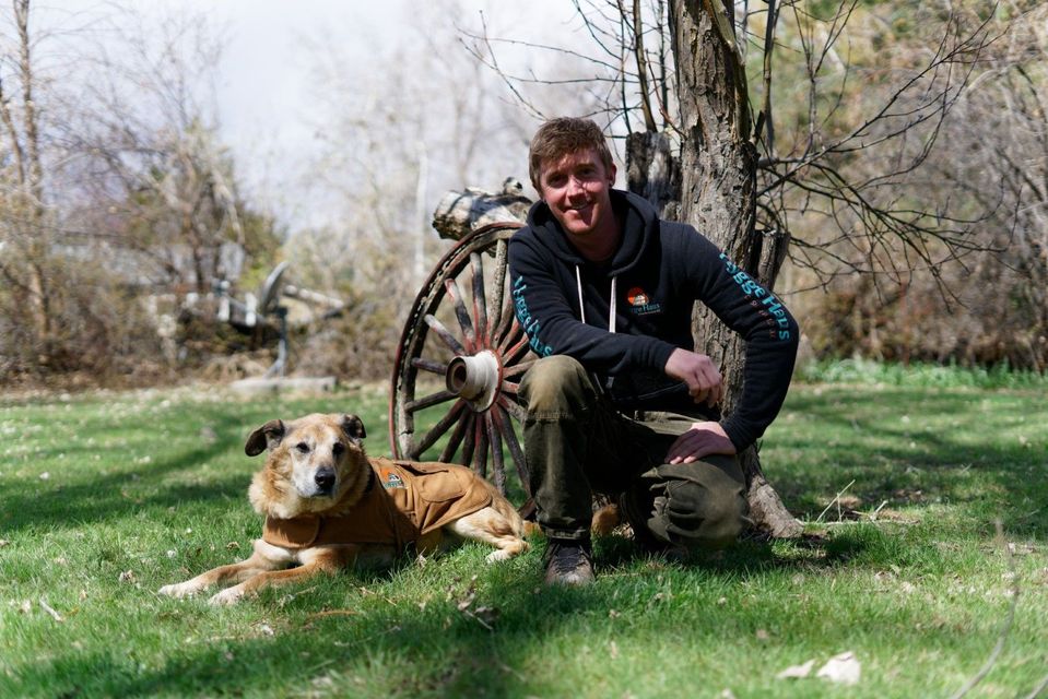 A man is kneeling down next to a dog in a field.