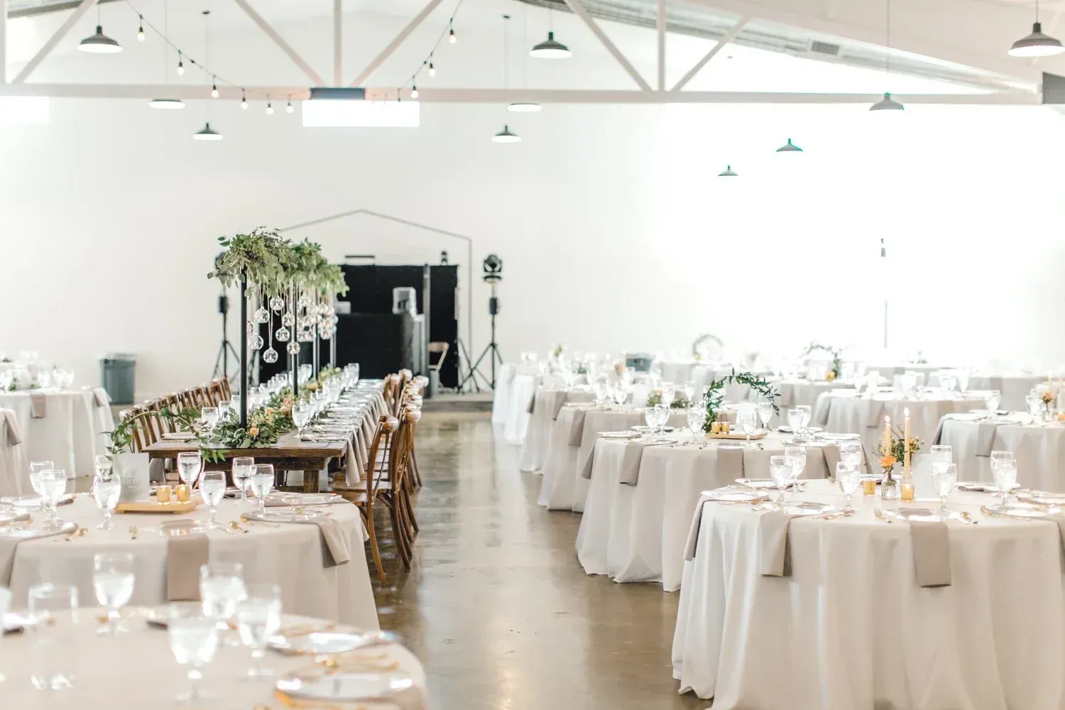 Elegant white-wrapped banquet tables in a bright wedding reception hall with floral and candle centerpieces