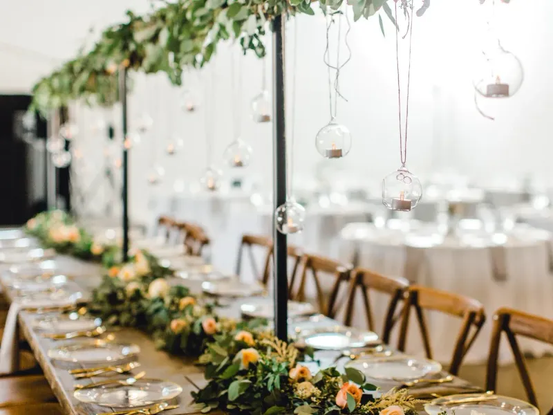 Elegant long banquet table with white linens, gold accents, greenery, and hanging glass pendant lights
