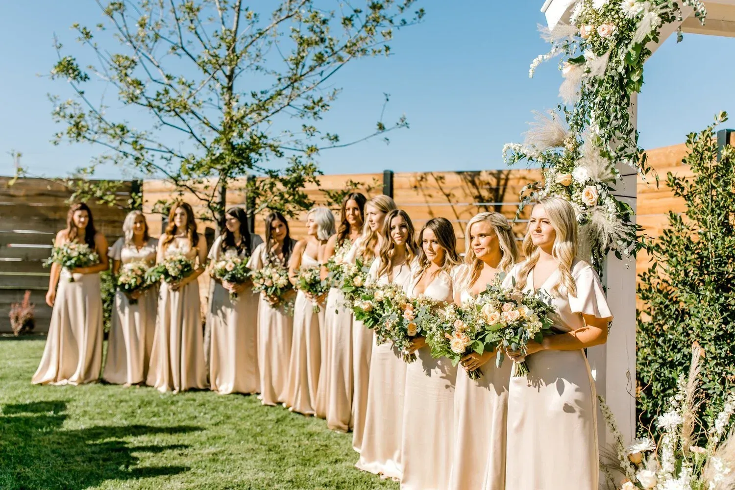 Bridesmaids in cream dresses holding green floral bouquets in an outdoor garden wedding scene