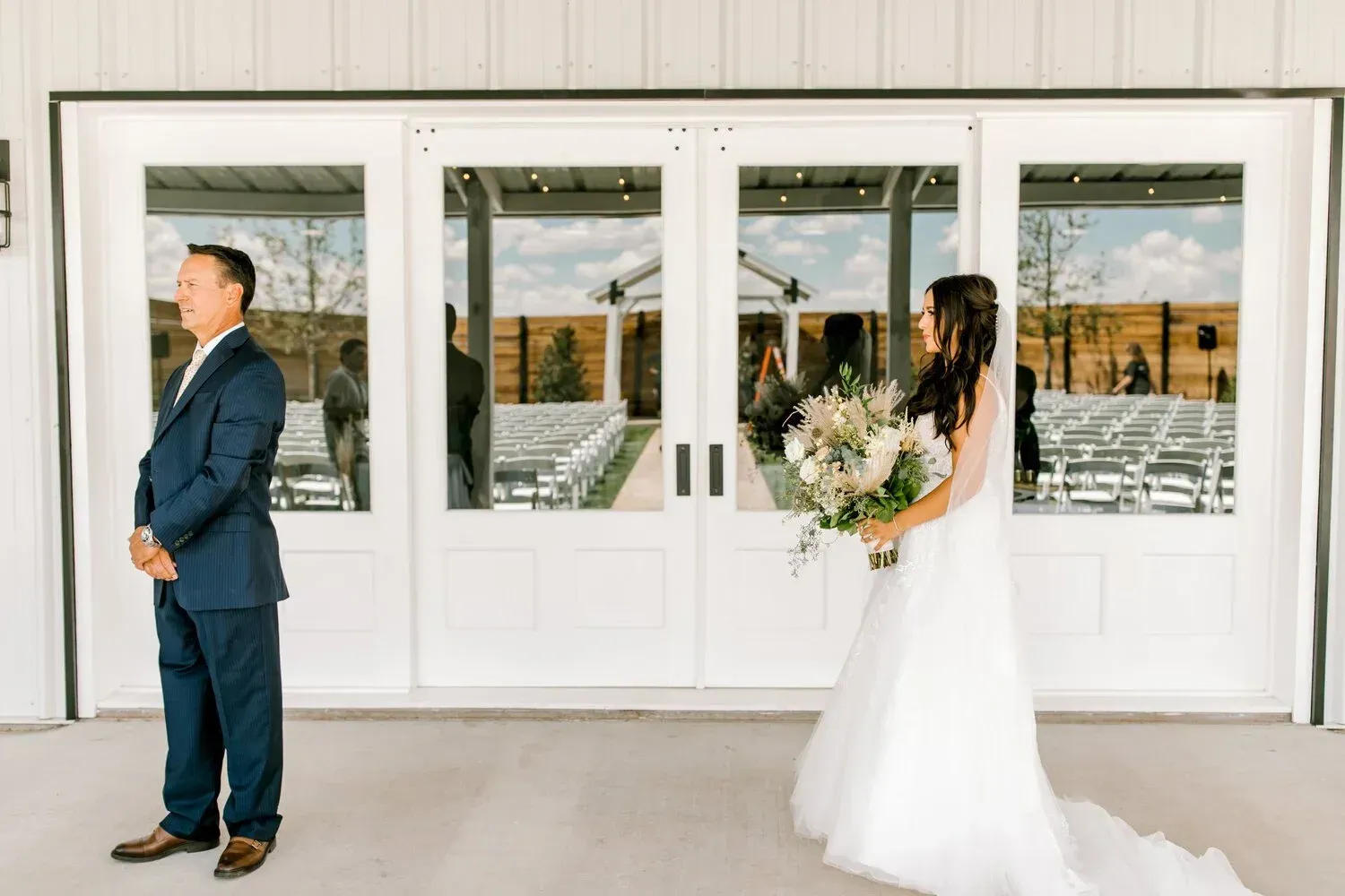 Bride in white gown holding bouquet near groom in navy suit outside white double doors
