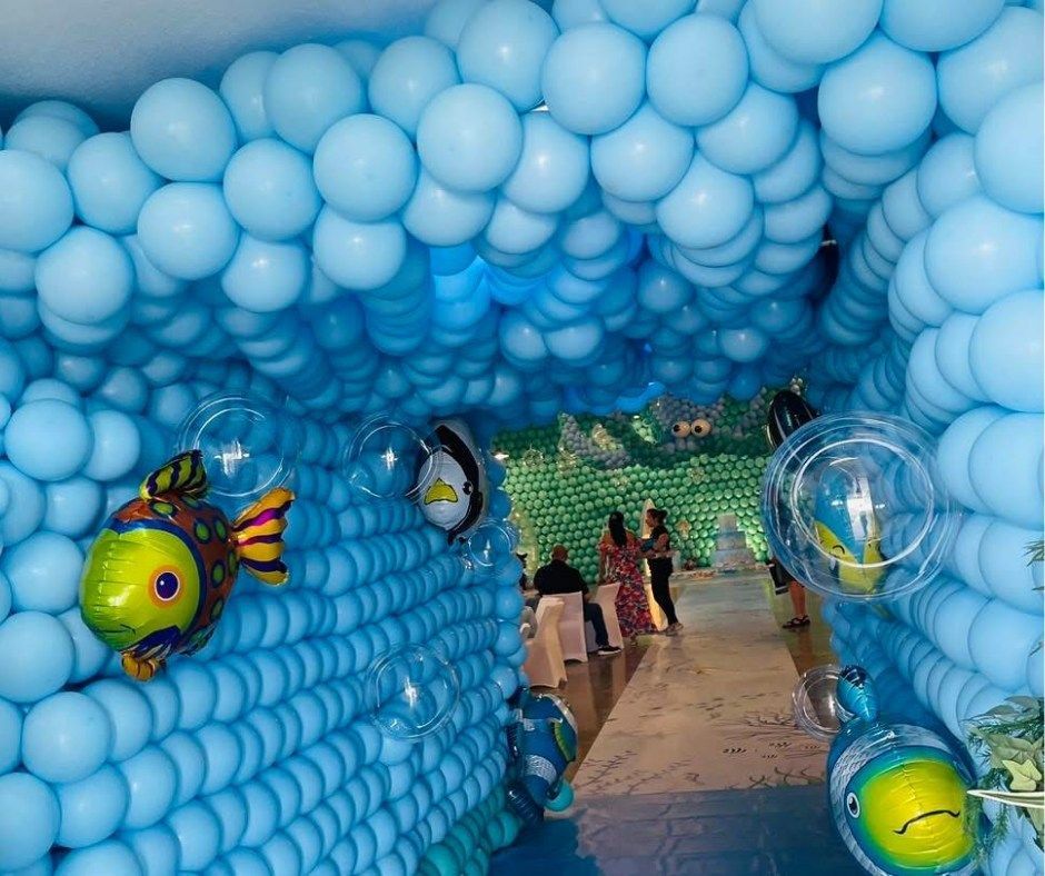 Blue balloon tunnel with hanging fish decorations and people walking through to a bright opening