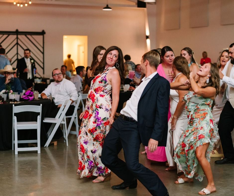 Guests dancing at a reception, with women in floral dresses and a man in a dark suit in the foreground